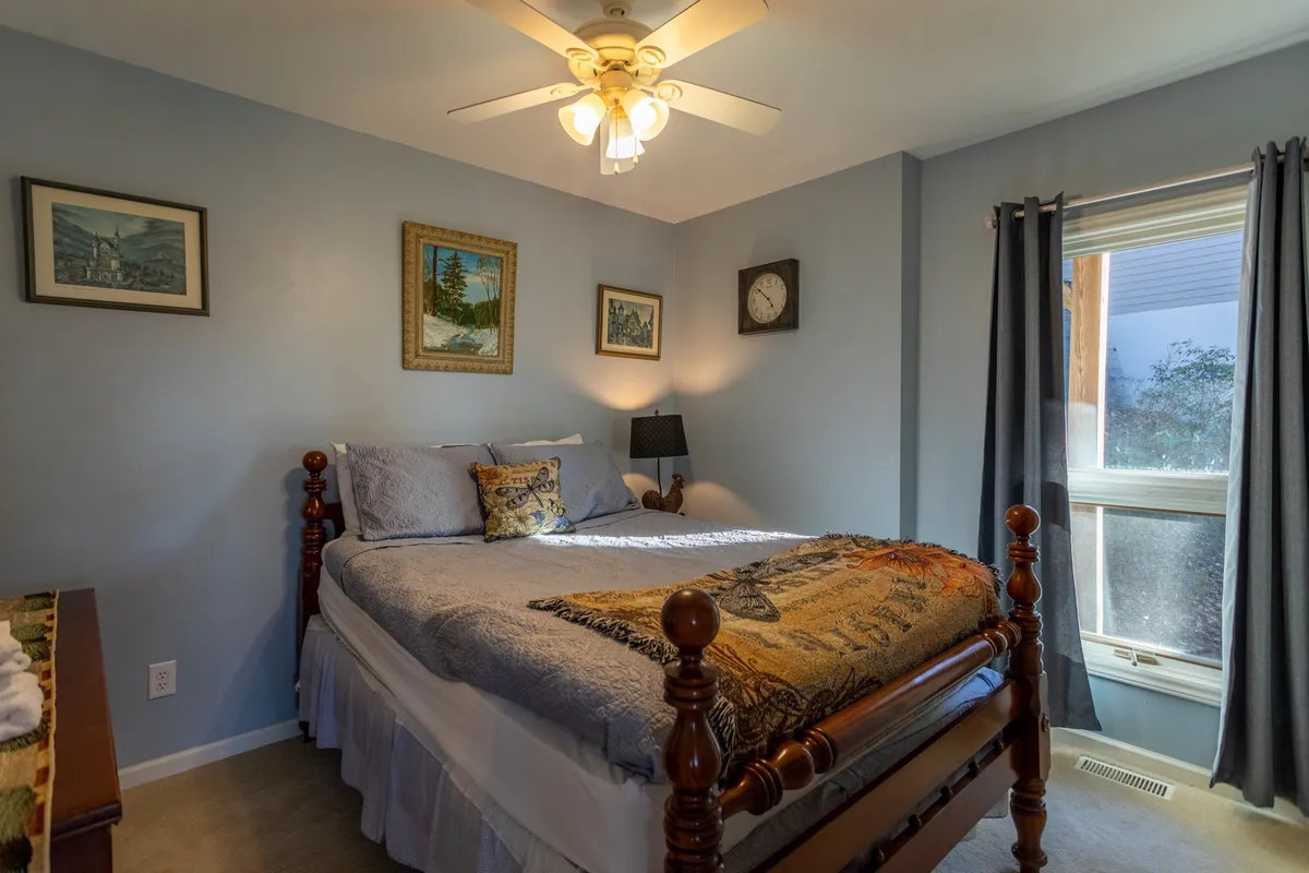 A warmly decorated bedroom with a plush bed, decorative bedding, soft wall art, a nightstand with a lamp, and a window letting in gentle light. The ambiance is calm and inviting, perfect for relaxation and quiet nights.