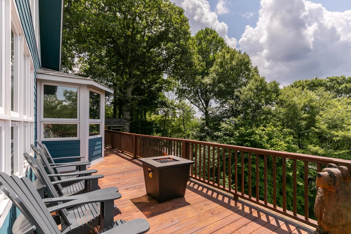 A tranquil scene featuring a generous deck area with comfortable seating, a fire pit, and a backdrop of surrounding trees. The space is ideal for socializing, enjoying meals outdoors, and relaxing after a day of exploring local attractions.