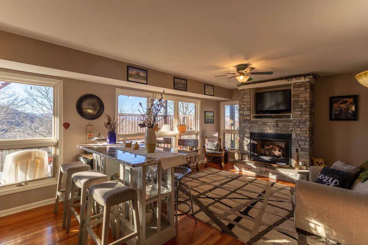 This image captures a welcoming living area featuring a cozy fireplace, expansive windows with scenic views, a bar counter, and ample comfortable seating. The space exudes warmth and is ideal for gathering with friends or loved ones, relaxing by the fire, or enjoying a drink together.