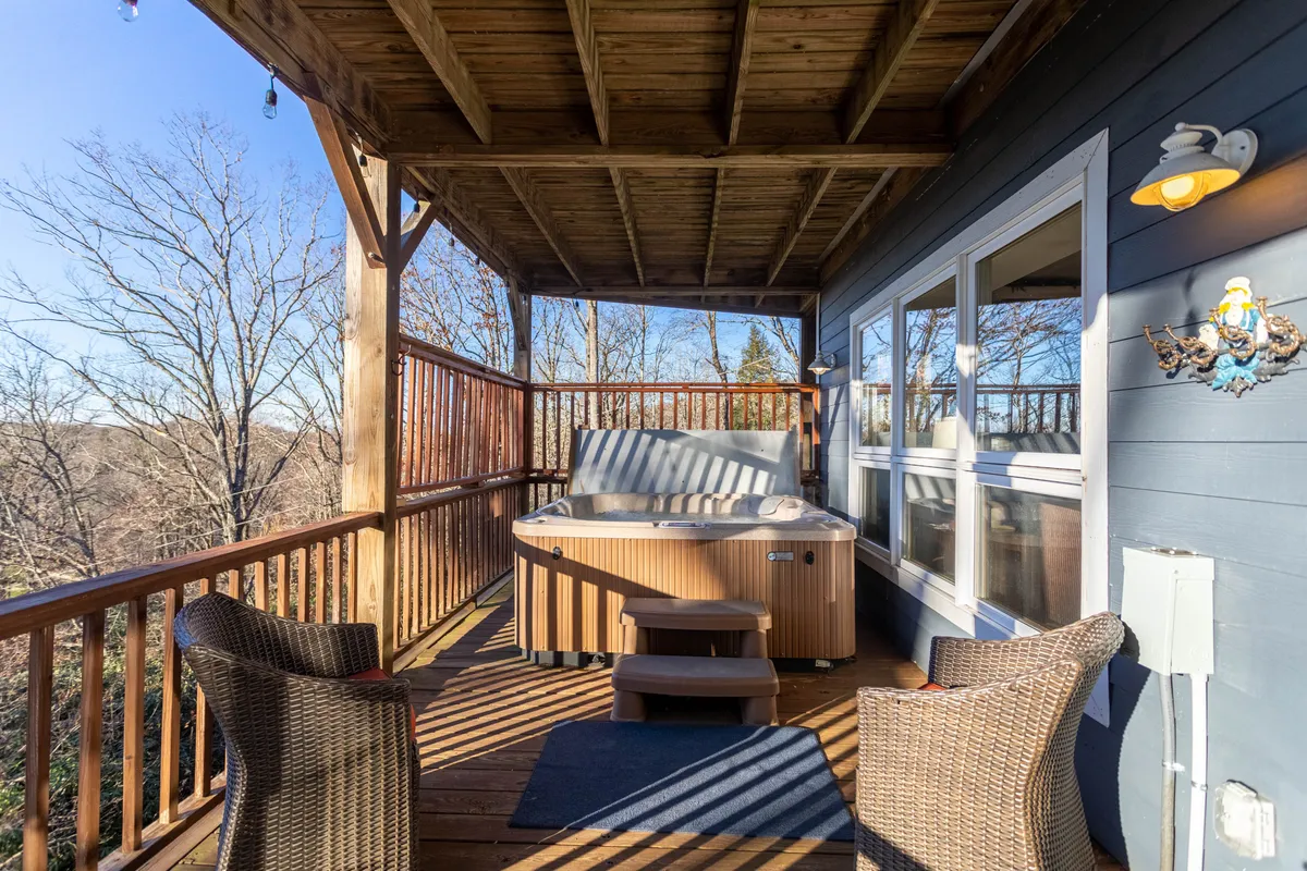 An inviting exterior view of the hot tub set on a wooden deck, surrounded by trees. There is also a seating area, making it perfect for groups to relax outdoors, regardless of the weather.