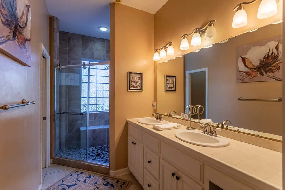 A modern, sparkling bathroom with double vanity sinks, glass-enclosed shower, and elegant wall art. Clean lines and ample lighting convey a sense of luxury and ease of use.