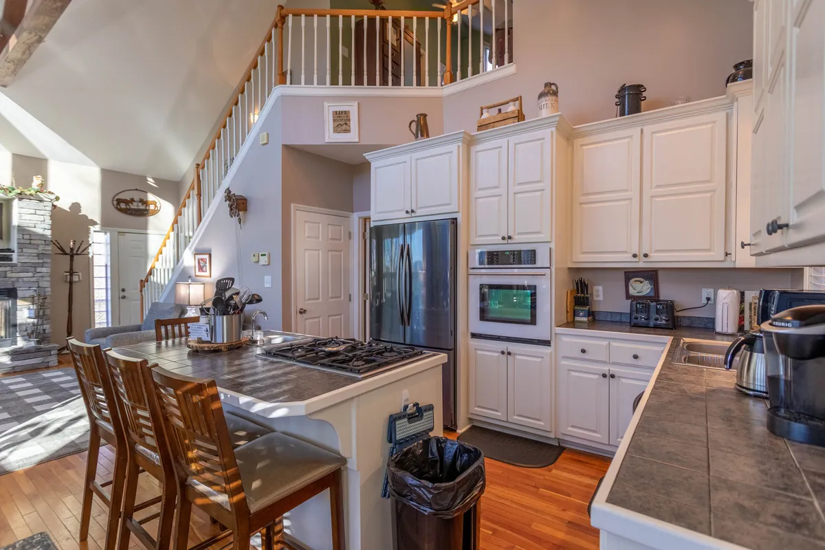 This bright interior showcases a modern kitchen island with stainless steel appliances, a staircase leading upstairs, and natural light pouring in. The area provides plenty of space for cooking, entertaining, and group celebrations.