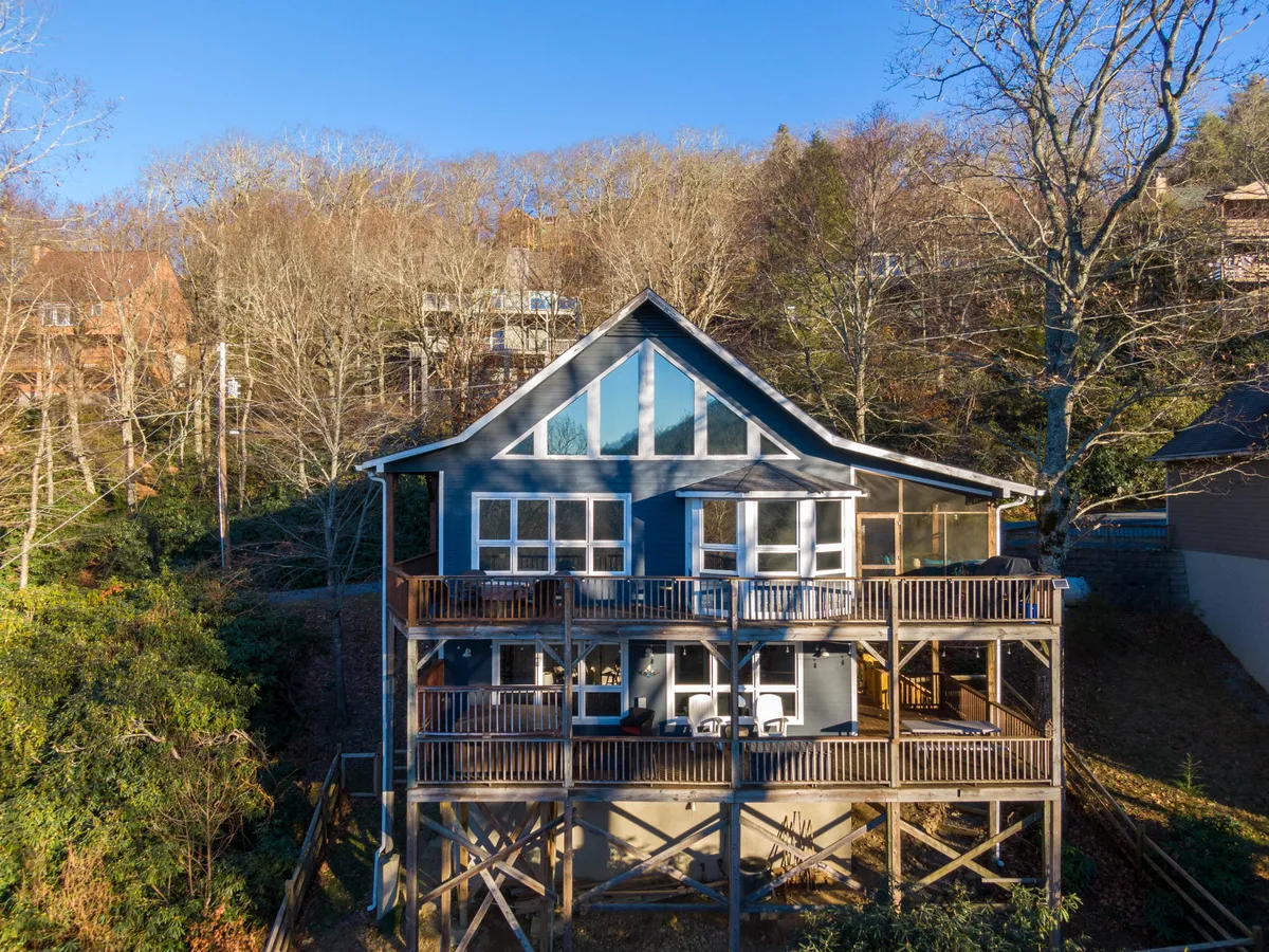 This photo captures the home’s exterior with large windows and an inviting deck area. The serene setting is surrounded by trees and open sky, offering a glimpse of the broader natural environment and outdoor gathering spaces.