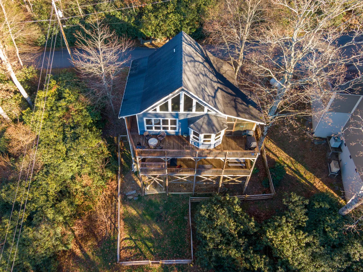 A wide exterior shot highlights the large deck, bay window, and the surrounding wooded landscape, ideal for family gatherings, outdoor lounging, and appreciating nature.