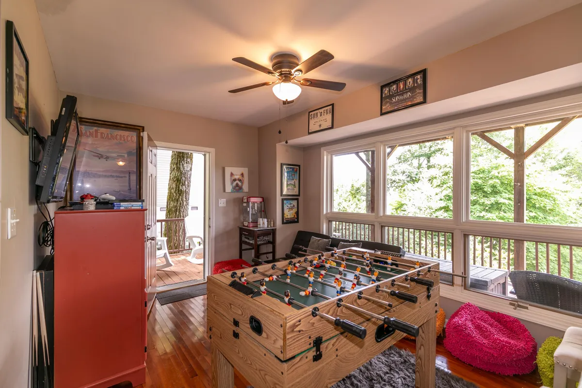 This playful and relaxed interior scene features a foosball table near large windows, a colorful bean bag, and comfortable seating. The bright natural light and spacious layout suggest a welcoming environment for guests of all ages to gather, socialize, and enjoy activities together.