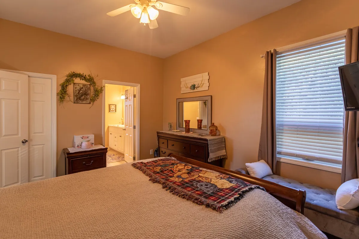 A cozy bedroom featuring a comfortable bed with a textured blanket, a classic wooden dresser, and a window with curtains that let in soft natural light. The neutral color palette and inviting decor create a restful atmosphere.