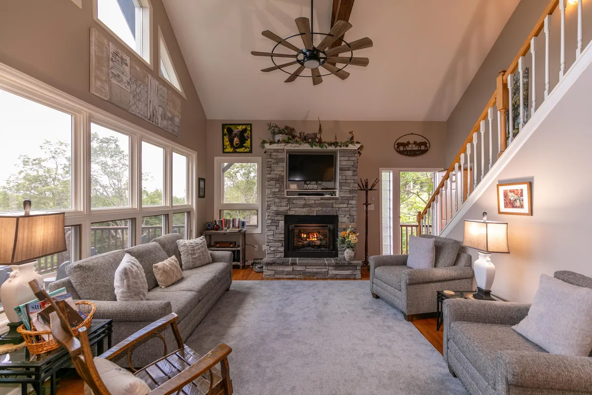 A lower level living room featuring a striking stone fireplace, large windows that flood the room with natural light, and comfortable seating—ideal for family gatherings or quiet relaxation after a long day.